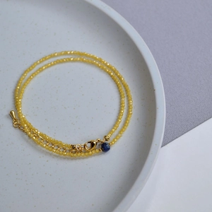 Detail of yellow crystal beaded necklace with golden clasp and blue charm on ceramic tray