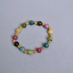 Close-up of handmade colorful tourmaline beads with gold flower spacers on a grey surface