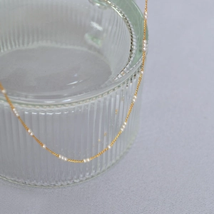 Détail d'un collier élégant en laiton doré avec mini perles sur verre strié