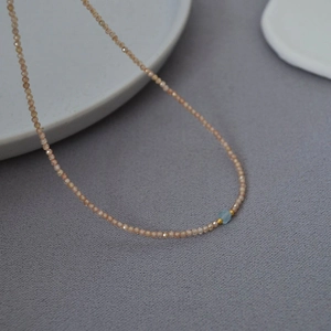 Detail of beaded necklace with faceted champagne pink beads and a blue central stone