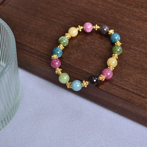 Macro view of multi-color tourmaline beads with gold flower spacers on wood stand