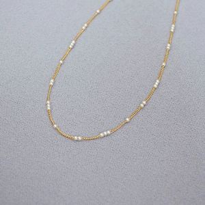 Détail de mini perles espacées sur une fine chaîne en laiton plaqué or pour femme