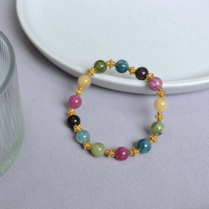 Handmade colorful tourmaline beaded bracelet with gold cross accents on a white plate