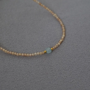 Detail of beaded necklace featuring pink round beads and a blue square zircon stone
