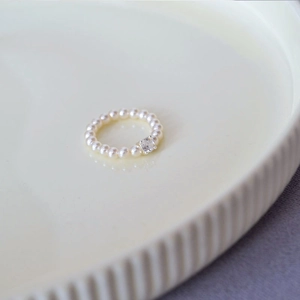 Macro shot of an elegant pearl ring featuring a square clear crystal on an off-white ceramic dish