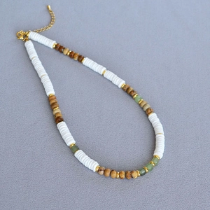 Detail of bohemian necklace featuring white shell discs, brown wood beads, and green stones