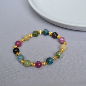 Detail of colorful tourmaline beaded bracelet with golden floral petal spacers on light grey background