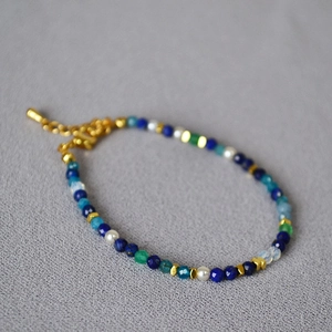 Lapis lazuli and crystal beaded bracelet with gold lobster clasp on grey textured background