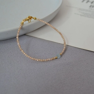 Close-up of minimalist beaded bracelet with pink faceted stones and gold lobster clasp