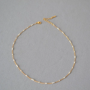 Détail de l'élégante chaîne en laiton doré avec petites perles et fermoir mousqueton