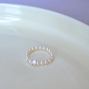 Elegant pearl beaded ring with a sparkling square-cut crystal center on a ceramic plate