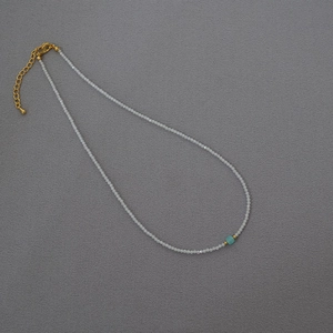 Detail of beaded necklace with translucent grey stones, turquoise bead and gold clasp