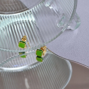 Dettaglio di orecchini a bottone quadrati in smalto verde acqua con bordi dorati su vetro