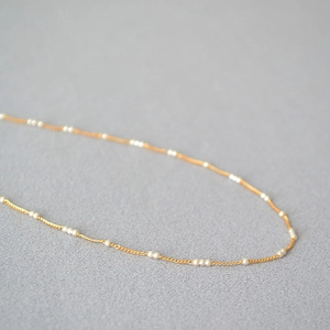 Gros plan d'un collier élégant en laiton doré avec de petites perles blanches fines