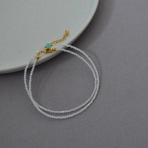 Detail view of dainty white beaded necklace with gold lobster clasp and turquoise accent bead