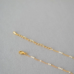 Détail du collier en laiton doré avec fermoir mousqueton et petites perles sur chaîne fine