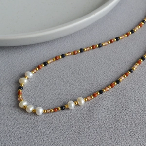 Detail of baroque pearl necklace with blue and gold sandstone beads on textured fabric
