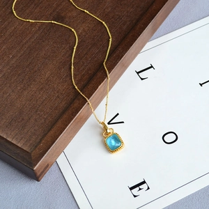 Collier vintage doré avec pendentif carré en cristal bleu sur un plateau en bois chic