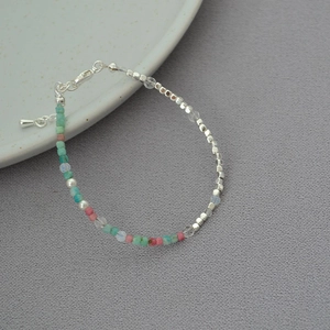 Detail of beaded necklace with pastel stones and silver metal cubes on soft gray fabric