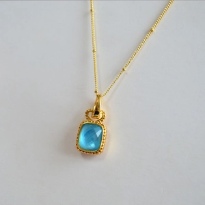 Détail du pendentif en cristal rectangulaire bleu clair avec monture dorée perlée