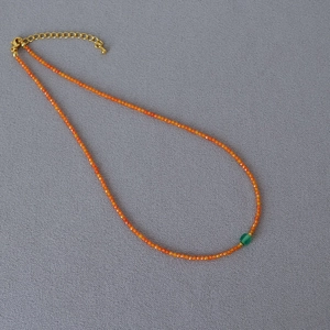Detail of orange beaded necklace with a central green hexagonal gem and gold clasp