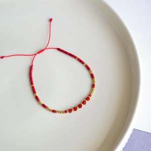 Detail of bohemian red beaded bracelet with golden accents and adjustable woven cord