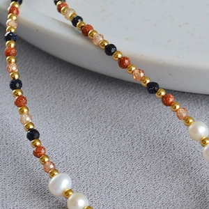 Detail of baroque pearl necklace with blue goldstone and gold spacers on a ceramic plate