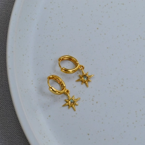 Detail of gold star drop earrings with moonstone inlay on a ceramic display tray