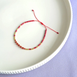 Detail of red Bohemian bead bracelet with gold accents and adjustable cord on ceramic plate