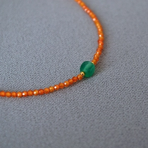 Detail of faceted orange beads necklace with translucent green stone and gold accents