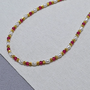 Macro shot of French style rice pearls and red corundum beads on a gold necklace