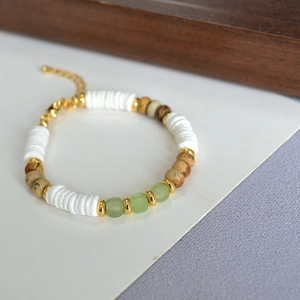 Detail of beaded necklace with white shell, brown stone, and green beads on gold chain