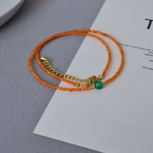 Detail of faceted orange beads necklace with a green focal stone and golden chain