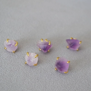 Macro detail of raw amethyst gemstones with gold-plated four-prong settings on fabric