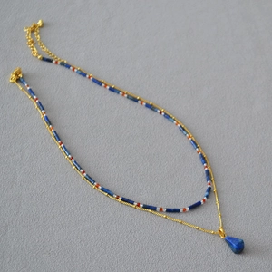 Detail view of double-layer beaded necklace with lapis lazuli teardrop pendant on gray fabric