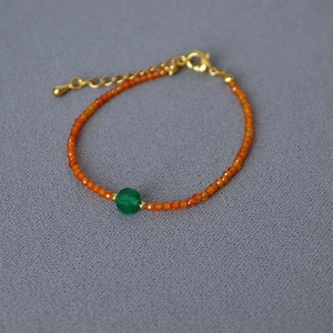 Detail of faceted orange beads bracelet with green center stone and gold lobster clasp