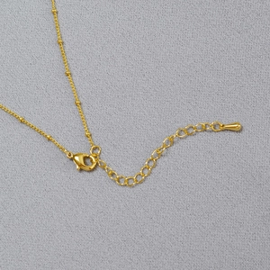 Detail of golden satellite chain with lobster clasp and teardrop pendant on gray fabric