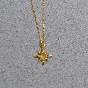 Macro detail of gold plated starburst pendant featuring a translucent gemstone inlay