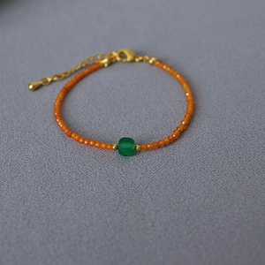 Detail of orange faceted beads and a green cube bead on a gold chain bracelet