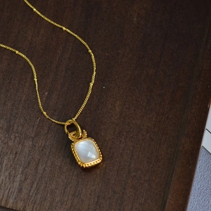 Collier rétro en laiton doré avec pendentif carré en nacre sur un plateau en bois
