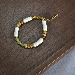 Macro view of beaded necklace featuring white shell discs and green faceted beads on wood