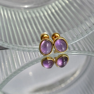 Macro view of oval amethyst studs with gold plated borders on glass reflective surface