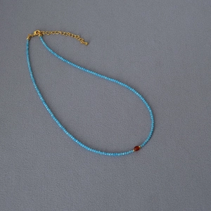 Detail of beaded necklace with blue faceted gems and amber center stone pendant