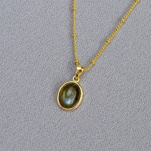 Gold oval labradorite stone necklace with delicate bead chain on textured background
