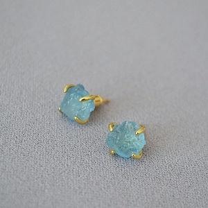 Detailed view of raw light blue gemstones in golden prong settings on grey fabric