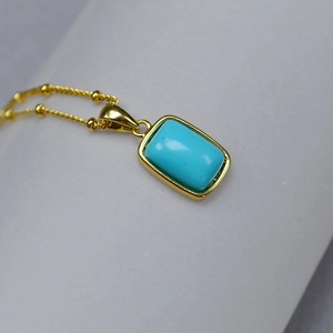 Macro view of a geometric gold-plated pendant with a rectangle turquoise stone and bead chain