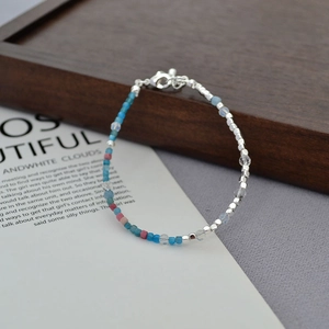 Detail of beaded bracelet with blue pink beads and silver metal cubes on wooden tray