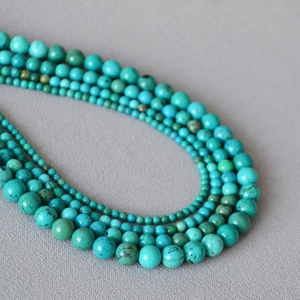 Close-up of turquoise beaded necklace featuring a gradient size design on grey fabric