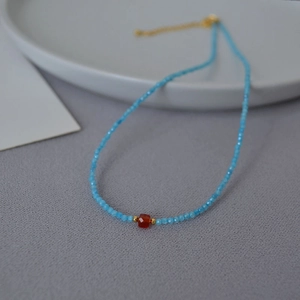 Detail of beaded necklace with light blue faceted beads and a red square stone focal point