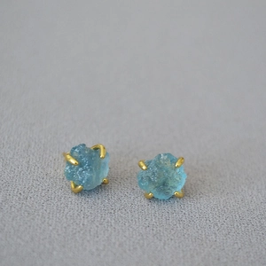 Macro view of light blue raw gemstone stud earrings with four-claw gold-plated setting